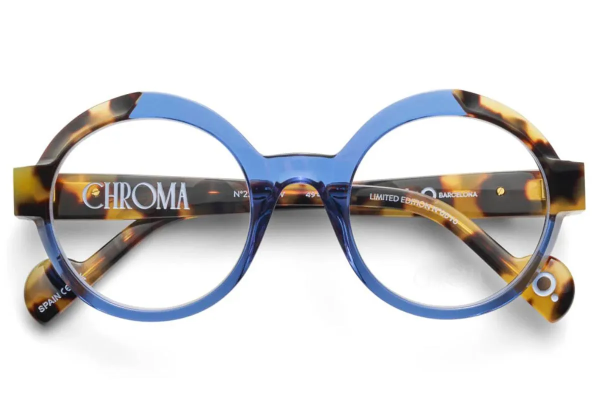 A pair of round eyeglasses with blue frames on the front and tortoiseshell-patterned temples, featuring the word “CHROMA” printed in white on the inside of the arm.